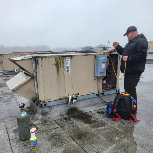 AMPM Heating and Cooling technician working on a large outdoor HVAC unit on a commercial building, with tools nearby